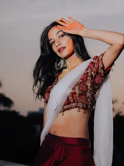 A post-Holi portrait, with the model's hand gently resting on her forehead, showcasing the lingering colors of the celebration against the evening sky.