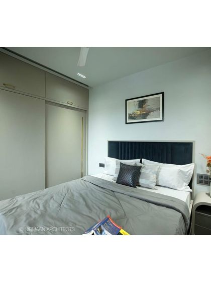 This master bedroom at Tulsi Heights uses a dark, moody theme to create a cozy and intimate atmosphere. The deep blue headboard and sleek wooden flooring contribute to the modern classic look.