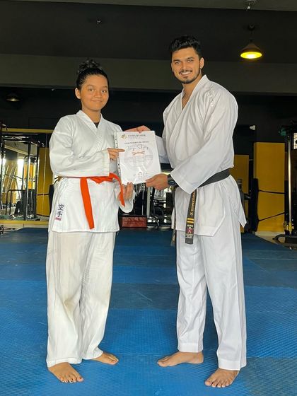 An orange belt student receives her certificate, marking her progress in the Shito-Ryu karate system.