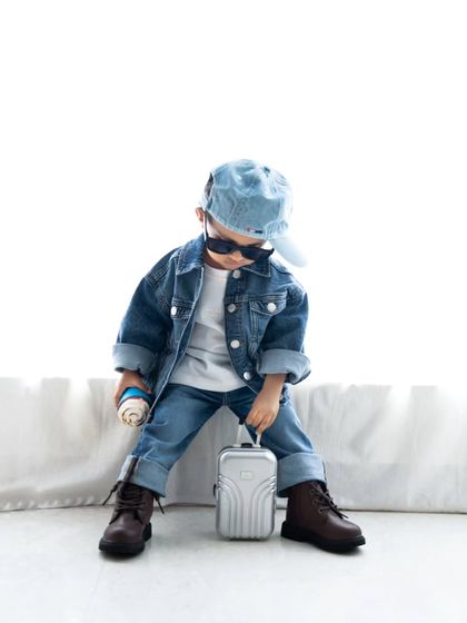 This little traveler is ready to go, holding a mini suitcase in his stylish photoshoot.