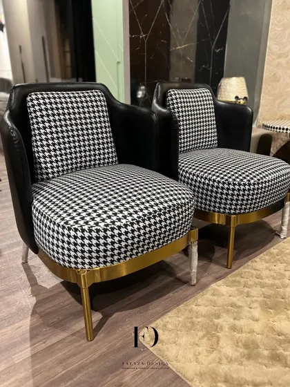 A pair of armchairs that make a graphic statement with a black-and-white houndstooth fabric. Paired with a black leather back and a gold-finished base, they are the definition of modern chic.