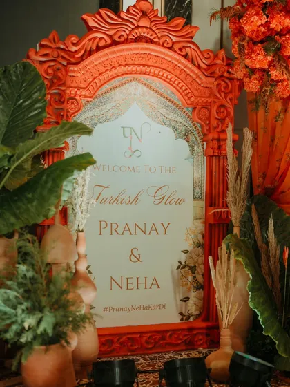 The welcome signage for the "Turkish Glow" Haldi, set in an ornate, custom-designed orange frame and surrounded by pampas grass and terracotta pots.