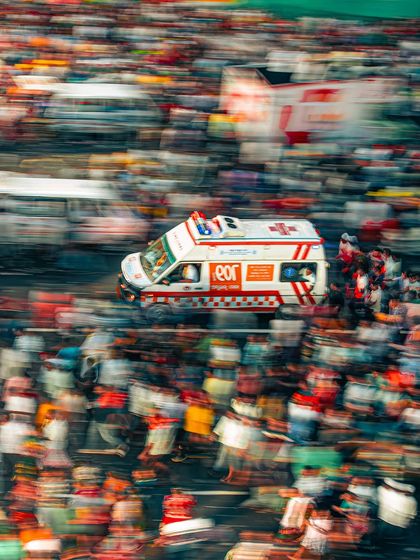 An ambulance with its lights flashing, captured with a slow shutter speed to create a sense of motion amidst the dense crowd of the Rath Yatra.