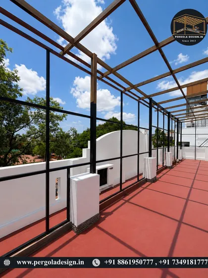 The bare frame of a large rooftop pergola under a clear blue sky. The red flooring is already in place, awaiting the finished structure.