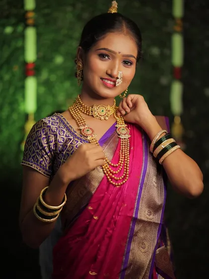 A happy bride adjusting her layered gold necklaces. This shot highlights the intricate details of traditional Maharashtrian bridal jewelry and the soft, glowing makeup that complements it.
