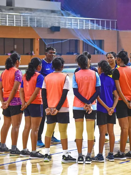 A behind-the-scenes moment with the women's handball team. The players are gathered in a huddle, listening intently to their coach, showcasing the strategic side of the game.