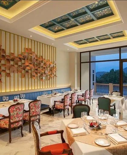 The interior of the IHCL Pilibhit-Haridwar restaurant, where a stunning wall art installation becomes the centerpiece. The design combines a long, comfortable banquette with elegant, custom-upholstered chairs for a luxurious feel.