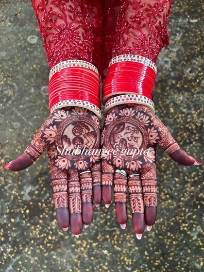 The beautiful dark stain of a Karwachauth mehndi, perfectly complemented by red bangles. This design features traditional portraits for the festival.