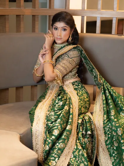 A full-length seated portrait, showcasing the rich fabric and intricate design of her saree. Her makeup is classic and elegant, perfect for a queen.
