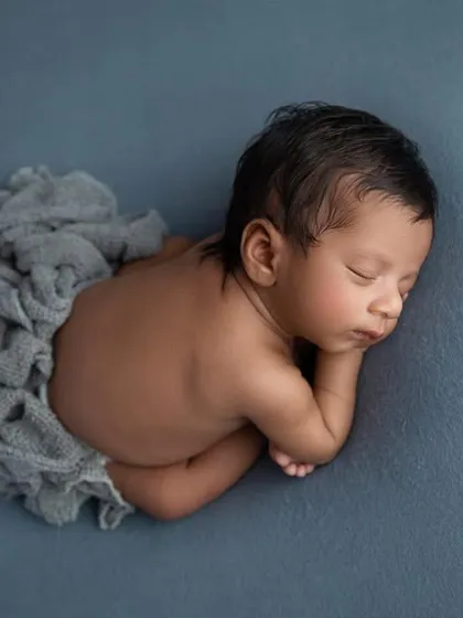 A top down view of the 'taco' pose on a blue grey backdrop, showcasing the baby's curled up form and the texture of the simple wrap.
