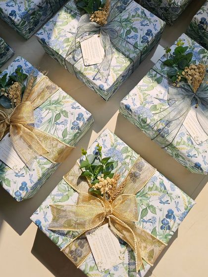 The sunlight catching these beautifully wrapped wedding return favors. It highlights the shimmer in the gold ribbon and the delicate details of the custom-printed paper.