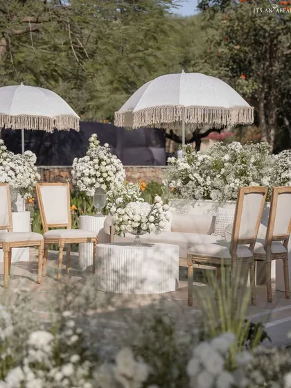 A chic lounge area at the lakeside Anand Karaj, with all-white furniture and fringed umbrellas providing a comfortable space for guests to relax.