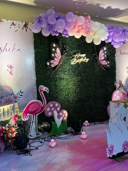 This is a duplicate of ID 6 and 88, 181. A whimsical garden theme combining butterflies, flamingos, and swans. The backdrop is a lush green wall with a neon sign, surrounded by pastel balloon garlands and cute props.
