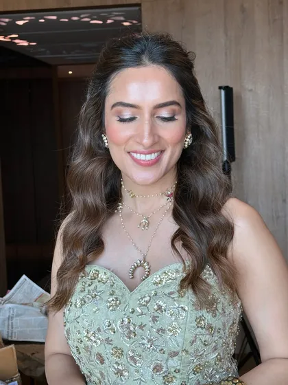 A smiling client with her eyes closed, showing off the soft glam makeup that pairs perfectly with her elegant half-up hairstyle.