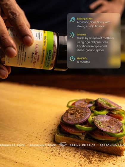 A hand sprinkling my Bombay Sandwich Masala over layers of fresh vegetables. This shot highlights the process and the key details: it's an aromatic, sour, and spicy blend made by mothers using traditional practices.