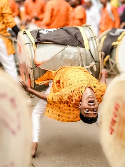 Capturing the peak of energy and devotion. This dynamic shot freezes a dhol player in a moment of acrobatic performance during a street festival, showcasing the raw power and spirit of the celebration.