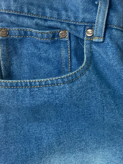 A close-up of the coin pocket and belt loop on a pair of light-wash denim jeans, showcasing the sturdy construction and hardware.