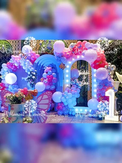 A vibrant and colorful butterfly-themed first birthday stage. This setup features a stunning mix of blue and pink balloons, illuminated butterfly props, and a light-up arch that frames the backdrop, creating a dreamy and magical atmosphere.