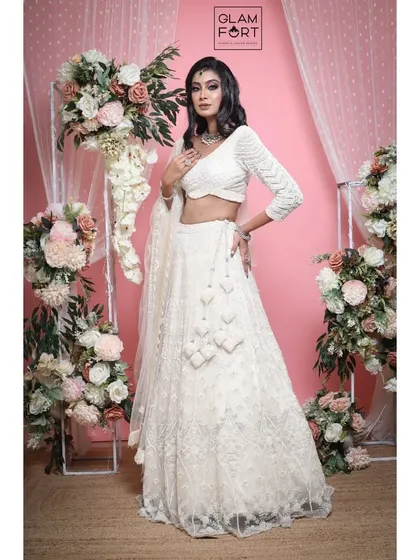 The full look against a beautiful floral backdrop. The makeup is dramatic, with a dark smokey eye that contrasts beautifully with the white outfit.
