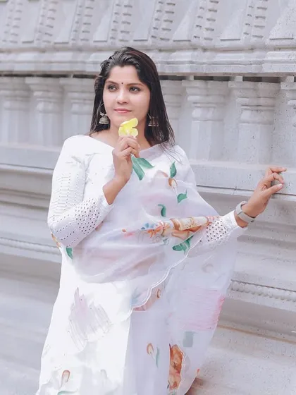 A close-up portrait against the white temple wall, focusing on the bride's gentle expression and the delicate floral pattern of her saree.