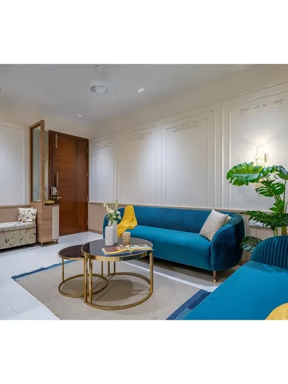 This angle highlights the full seating arrangement, with two curved teal sofas creating a conversational and inviting space. The simple rug and indoor plant complete the fresh, modern look.