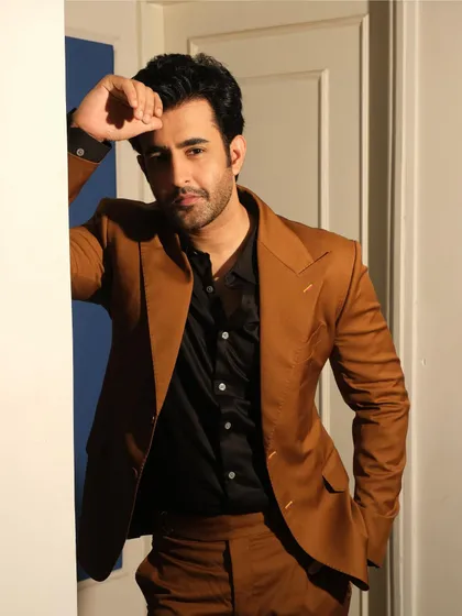 A closer view of the brown formal suit, showing how the broad lapel frames the look. Paired with a black shirt, the ensemble makes a sophisticated and powerful statement.