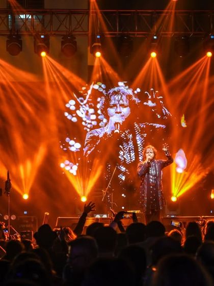 Bathed in orange light, our vocalist connects with the audience. A powerful shot from our NYE 2026 performance, highlighting the grand scale of the event.