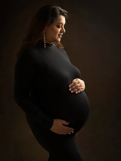 In the quiet of the studio, with just a simple black gown and soft lighting, a mother's strength becomes the entire story. This classic, minimalist maternity portrait focuses on the beautiful silhouette of pregnancy, creating a timeless piece of art.