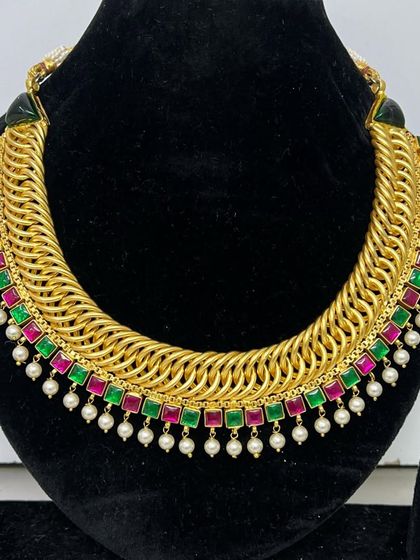 A bold gold-plated sutarla-style necklace. The thick, woven design is accented with pink and green stones and pearl drops, making it a true statement piece.