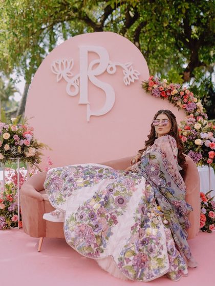 A stylish bride poses on a pink sofa at her carnival-themed event, looking cool and confident.