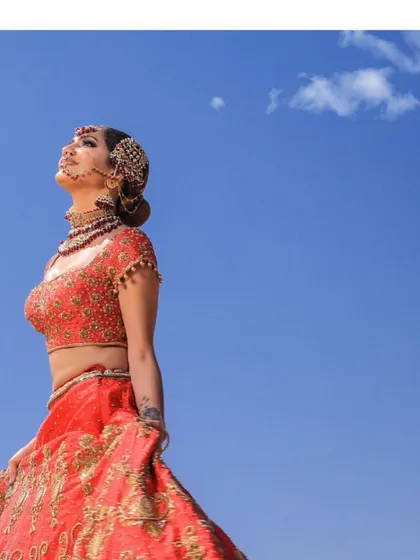 An ethereal portrait of the summer bride in her coral-red lehenga, looking up towards the sky. The intricate zardosi work glimmers in the sunlight.