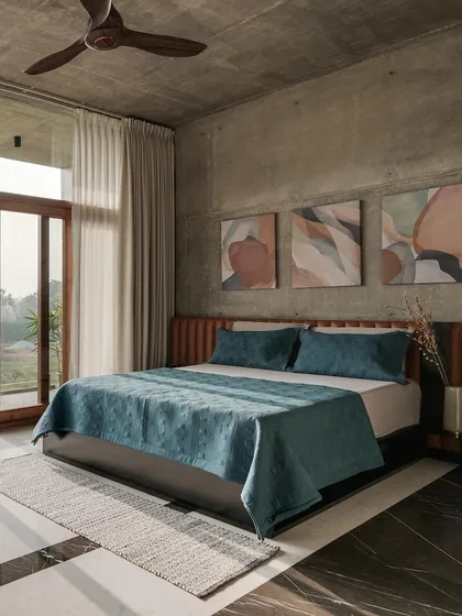 This bedroom combines the rawness of an exposed concrete ceiling and walls with the warmth of a leather headboard and wooden flooring. The full-height windows open onto a balcony, offering expansive views of the surrounding landscape.