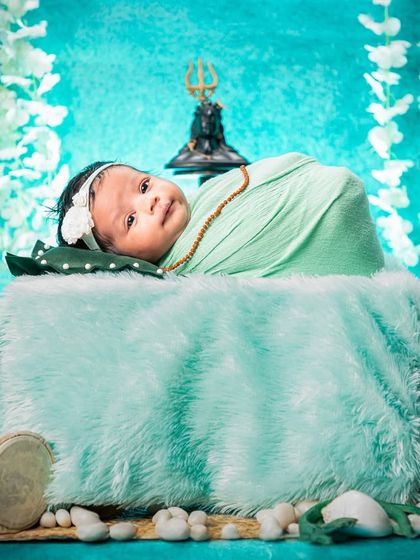 A different angle of our popular Maha Shivratri setup, this shot shows the baby looking curiously at the camera. The composition includes the Trishul, damru, and hanging flowers for a complete thematic look.