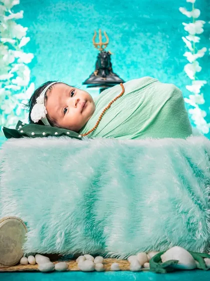 A different angle of our popular Maha Shivratri setup, this shot shows the baby looking curiously at the camera. The composition includes the Trishul, damru, and hanging flowers for a complete thematic look.