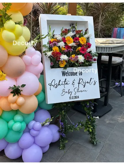 A unique welcome sign for a 'Baby in Bloom' shower, featuring a 3D frame filled with fresh flowers. This piece serves as both a sign and a beautiful floral art installation.