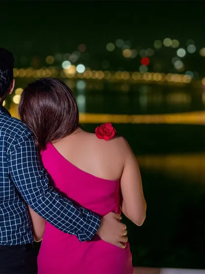 Overlooking the city lights reflecting on the water. This is a classic romantic pose that captures the beauty of the location and the quiet connection between the couple.
