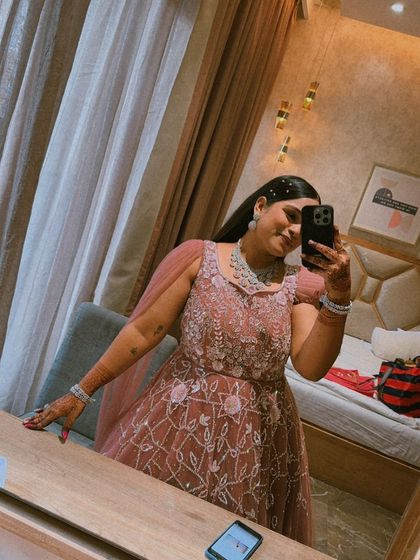 A client taking a selfie in a dusty pink embroidered gown, showing off the beautiful details and her stunning makeup.