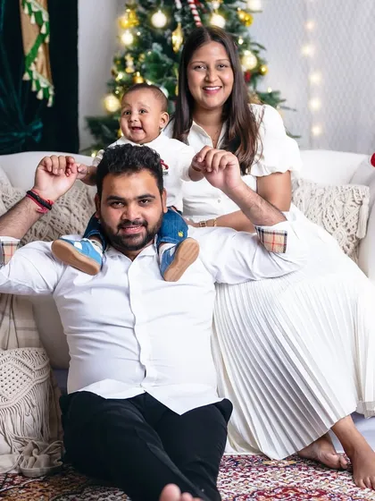 A happy family moment with their little one on dad's shoulders, all smiles in front of the beautifully lit Christmas tree.