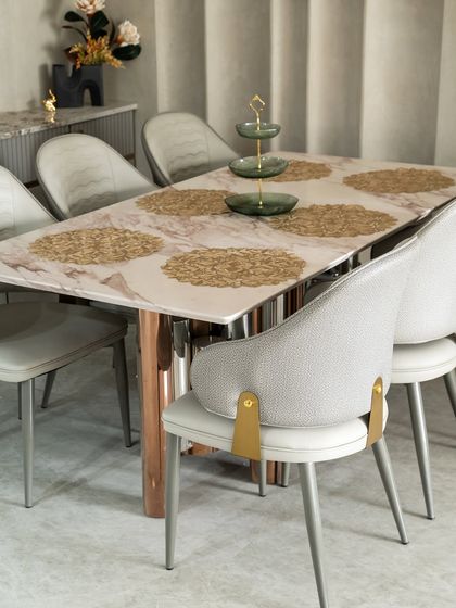 This dining space exudes quiet luxury through a harmonious blend of textures and tones. The marble tabletop with soft pink veining and rose-gold metallic legs elevates the entire setup.