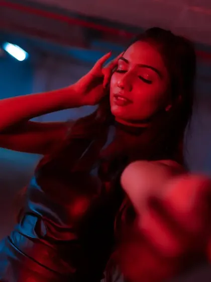 A sensual and moody close-up, with the model's hand reaching towards the camera, bathed in a mix of red and blue light.