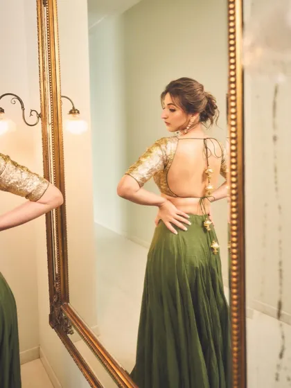 A look in the mirror before the show. This shot captures the back detail and the stunning silhouette of Dhvani Bhanushali's gold and olive green lehenga by Heena Kochhar.