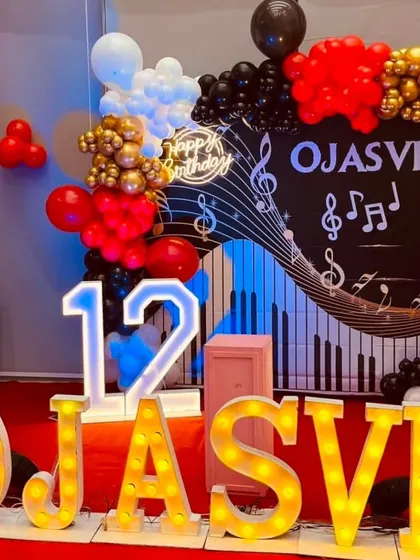 A music-themed 12th birthday party. The backdrop features a keyboard and music notes, with red, black, and gold balloons and the birthday girl's name in large marquee letters.