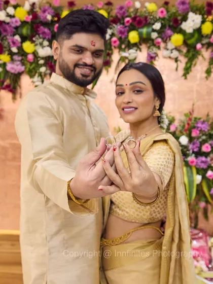 A smiling couple presenting their engagement rings against a vibrant floral background. I focus on their happy expressions and the details of their traditional attire.