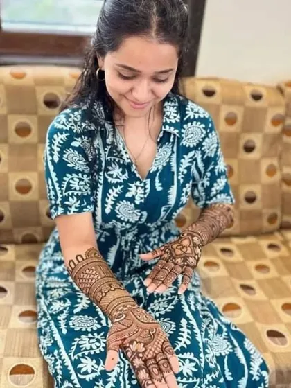 A lovely client admiring her freshly applied mehandi. The design is a traditional full-hand pattern with peacocks and intricate details.