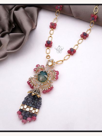 A majestic pendant necklace featuring a large blue-green gemstone, ruby beads, and polki diamonds. This piece is a work of art, perfect for clients seeking one-of-a-kind treasures.