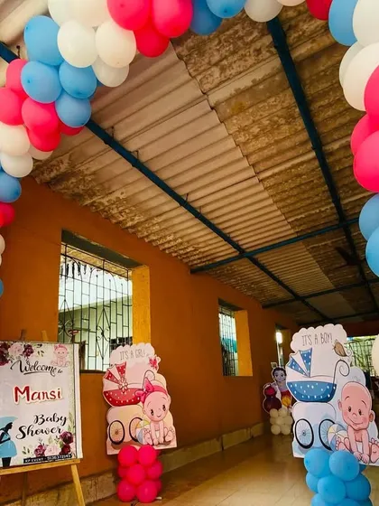The entrance to a baby shower, marked by a pink, blue, and white balloon arch and a personalized welcome sign.