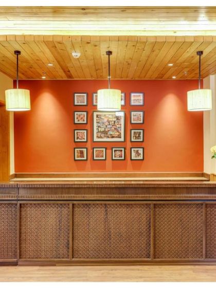 The reception desk at Janjehli Resort features intricate wooden carving and is set against a bold red wall adorned with traditional Chamba Rumal artwork. This immediately immerses guests in the local culture.