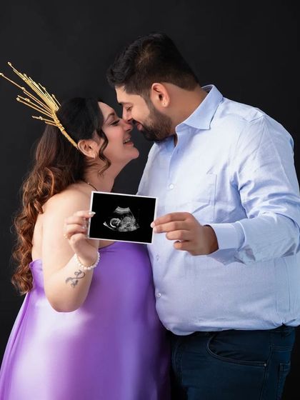 A creative and intimate shot featuring the sonogram. The couple is close to sharing a kiss, their first baby picture held between them, symbolizing the love that started it all.