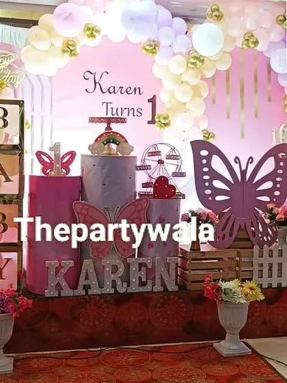 A grand stage setup for a "Fairy with Butterfly" theme. This includes a large fairy wing silhouette, "BABY" blocks, and a beautiful pastel balloon arch.
