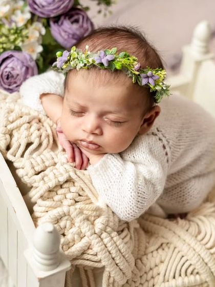 A detailed close-up of the baby sleeping in her floral bed. This angle highlights the delicate flower crown and the peaceful expression on her face.